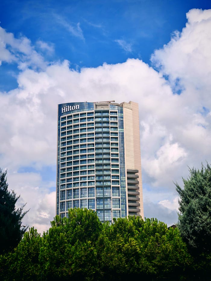 A modern Hilton hotel tower with blue sky and fluffy clouds creating a serene atmosphere.
